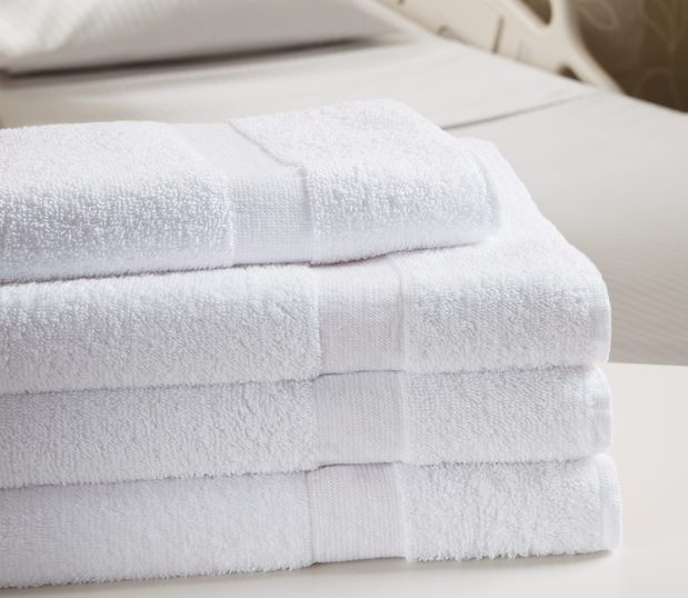 Our Double Duty Terry towels are shown here in a stack on a hospital bed. These hard working towels are soft enough for hotels and yet durable enough for hospitals.