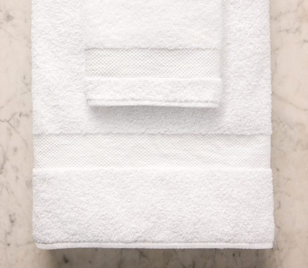 This is an image of a towel and hand towel supended from a towel rod. The EuroClassique bath towels are long-lasting towels.