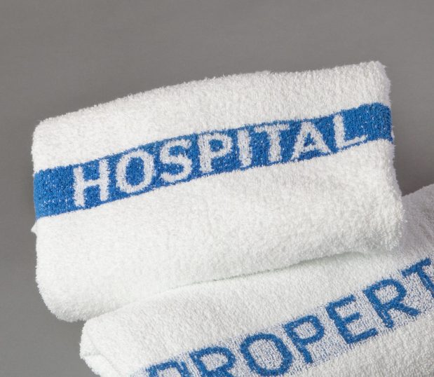 Hospital Property Basic terry helps discourage theft and helps facilities reduce towel loss and replacement costs. Shown here is a stack of towel towels that say Hospital Property in Blue.