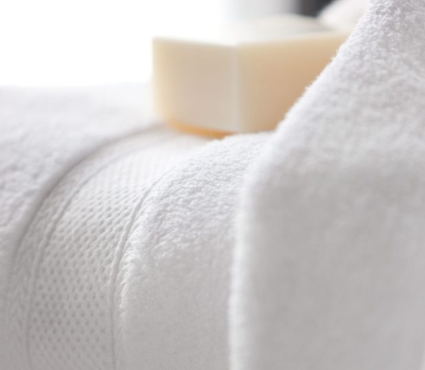 A detail shot of the Lynova® Microcotton Towels wide dobby border. An artisan soap is nestled on top the towel. These are the softest towels in hospitality.