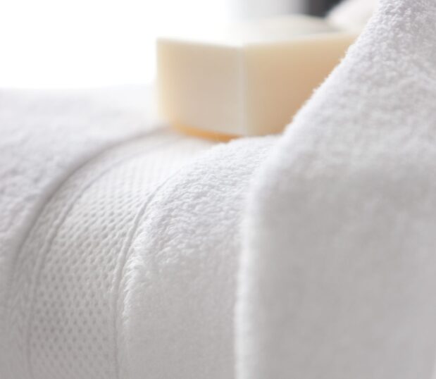 A detail shot of the Lynova® Microcotton Towels wide dobby border. An artisan soap is nestled on top the towel. These are the softest towels in hospitality.