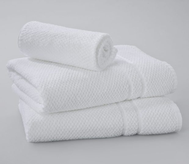 Photo of pique weave towels in a stack with a matching hand towel. Pique Weave Towels are unique jacquard towels. They have an overall texture and two thin decorative dobby borders for design effect.