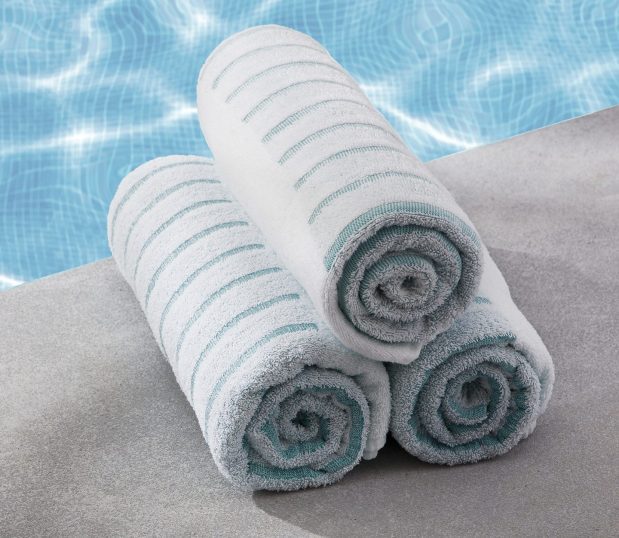 Three neatly rolled striped teal pool towels are stacked pool edge.