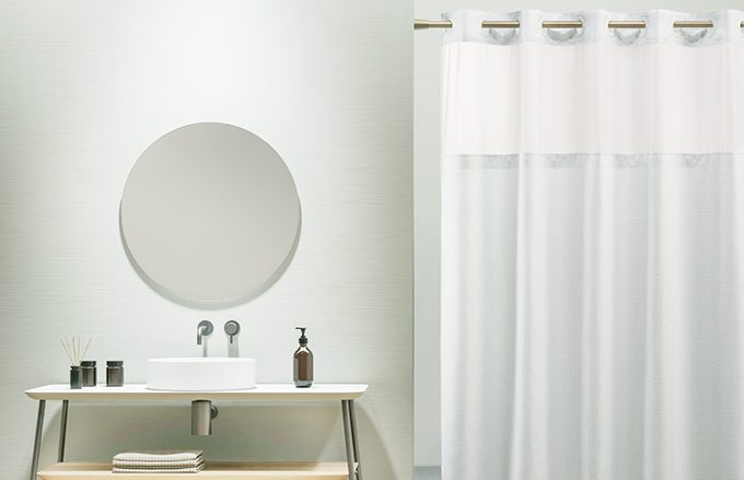 bathroom with round mirror over skink and vanity, next to a shower with white shower curtain