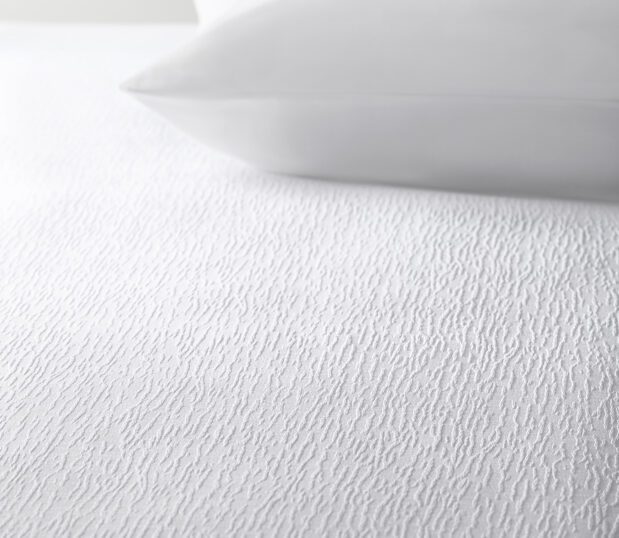 The white Impressions textural Crackle top cover shown on a bed with a white pillow.