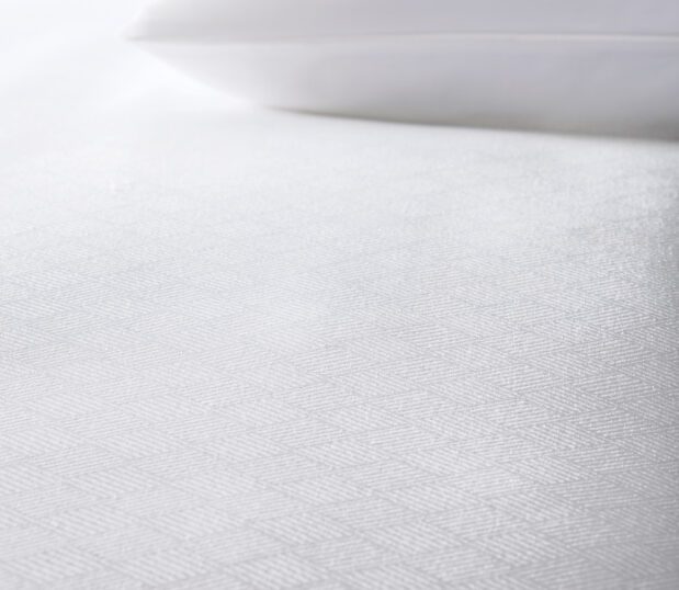 The white Impressions Solitaire top cover shown on a bed with a white pillow.