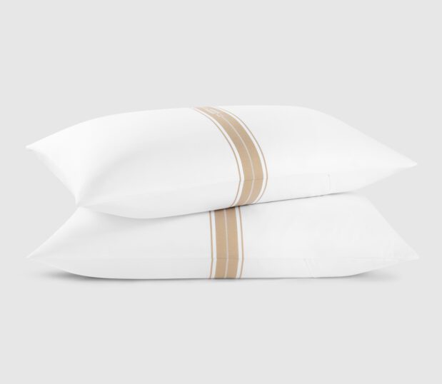 Two Concerto pillow cases with pillows are stacked on top of one another. The design is a band of stripes: narrow stripe, wide stripe, narrow stripe, wide stripe narrow strip. The Concerto shams are with with gold stripes.