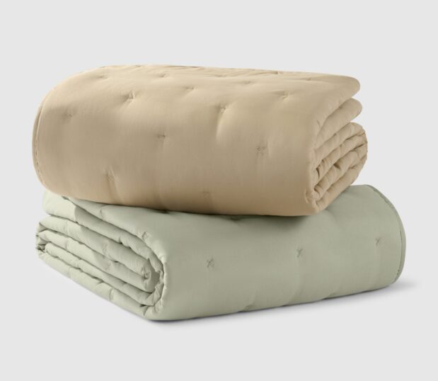 A stack of the Casa Quilted bedspreads are shown here in both colorways Sand and Eucalyptus.
